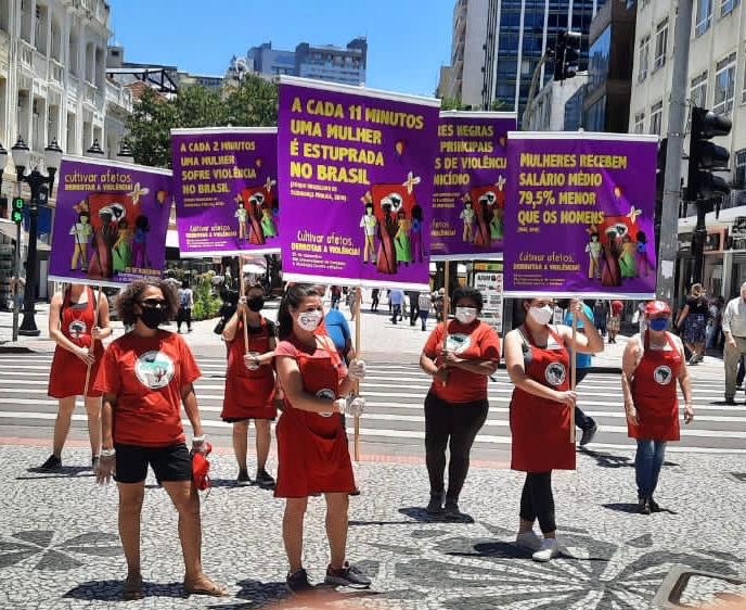 MST Women protesting at a city square holding banners that highlight that Four women are murdered every day in Brazil today. 