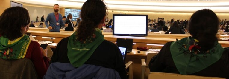 An image showing La Via Campesina's peasant leaders wearing the green LVC scarf and attending a UN session on Binding Treaty. The photo is shot from their back, so the faces cannot be seen.